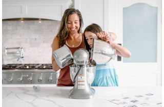 Mother and daughter pouring cake batter into a standing mixer in a kitchen