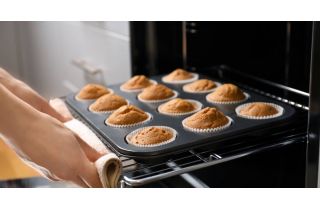 Someone using a towel to pull a pan of delicious, golden cupcakes in white liners out of a hot oven.