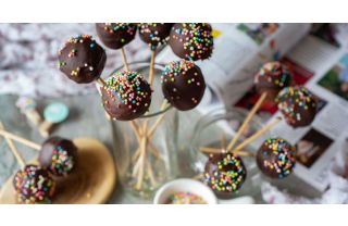 Clusters of cake pops with a chocolate coating and sprinkles displayed in glass jars and laid out on a table.